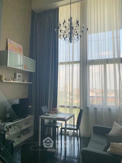 Modern living room with high ceilings, large windows, and elegant chandelier, offering a bright and airy atmosphere.