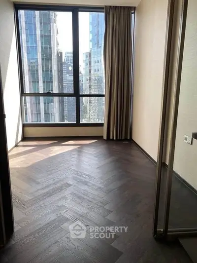 Bright room with large window and city view, featuring elegant dark wood flooring.