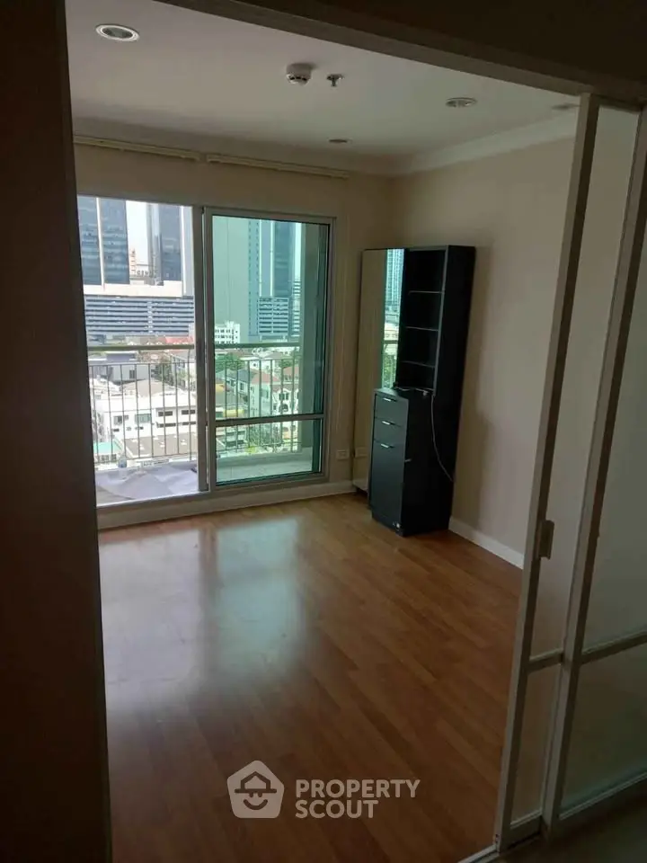 Spacious room with wooden flooring and city view balcony in modern apartment.