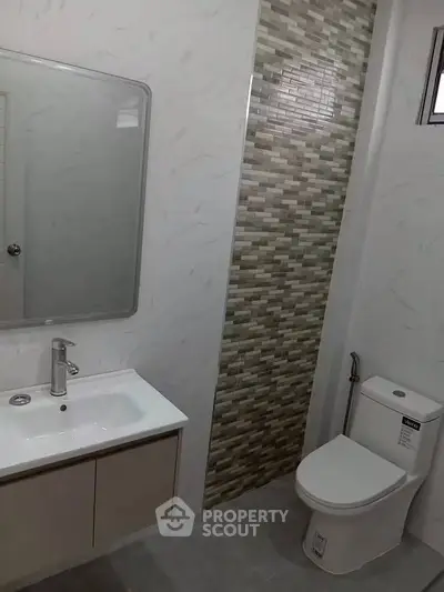 Modern bathroom with sleek sink and toilet, featuring stylish tile accents.