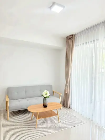 Bright modern living room with gray sofa and wooden coffee table, featuring large window with sheer curtains.