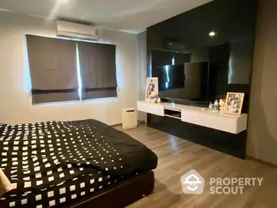 Modern bedroom with sleek black and white decor, featuring a large TV and stylish furnishings.