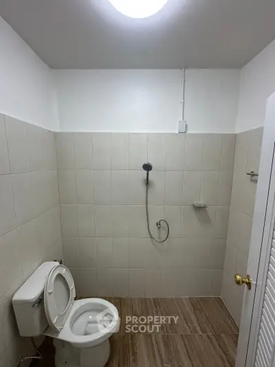Minimalist bathroom with tiled walls and floor, featuring a toilet and shower area.