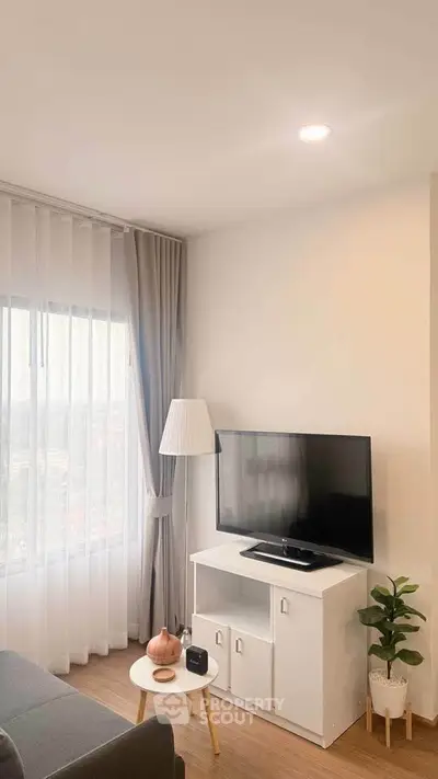 Modern living room with TV, stylish decor, and large window with sheer curtains.