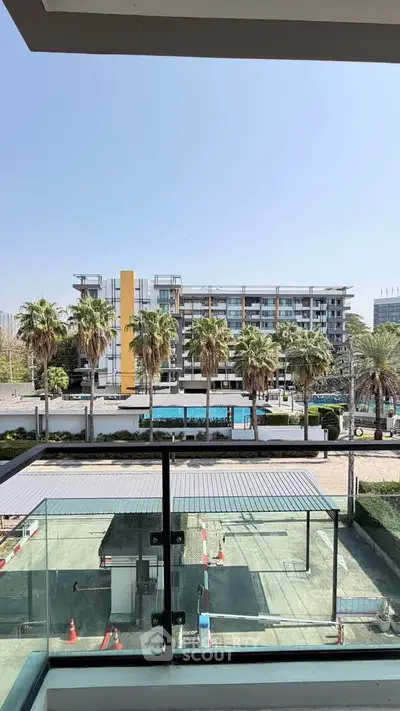 Modern apartment balcony with glass railing overlooking pool and palm trees, offering serene urban living.