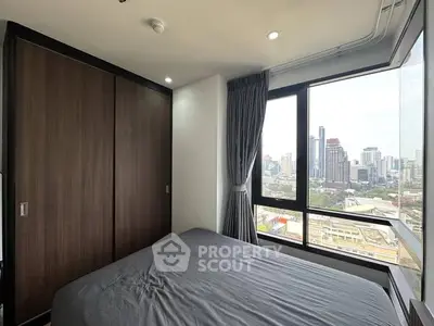 Modern bedroom with city view and large windows in high-rise apartment.