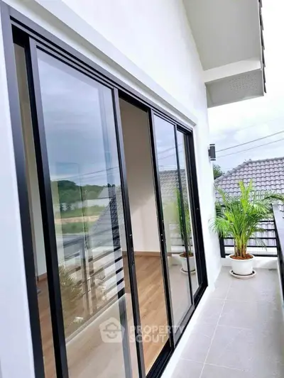 Modern balcony with sliding glass doors and potted plants, offering a serene view.