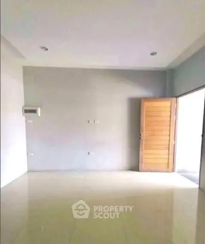 Spacious empty room with tiled flooring and wooden door, ideal for customization.