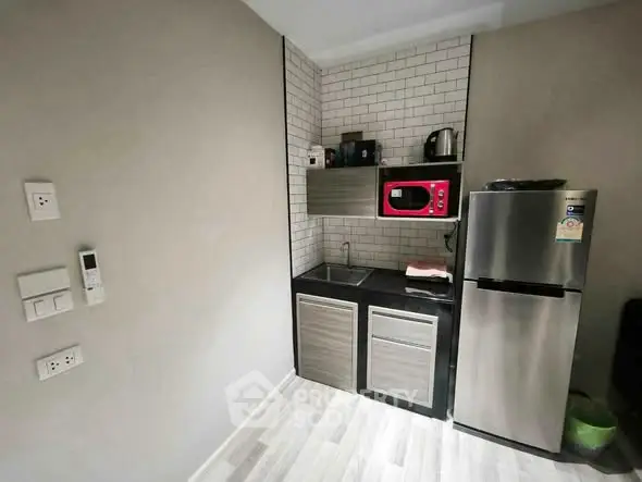 Modern compact kitchen with stainless steel fridge and red microwave in sleek apartment.