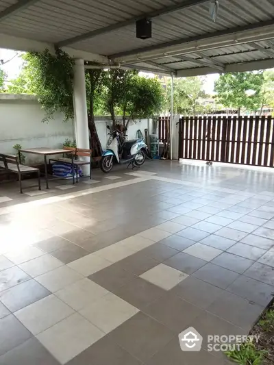 Spacious covered parking area with tiled flooring and scooter, ideal for vehicle storage.