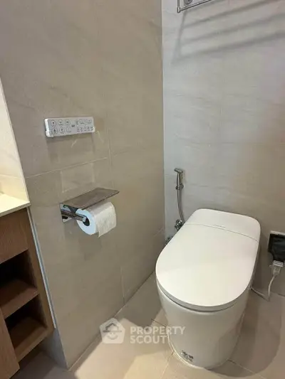 Modern bathroom with sleek toilet and beige tiles, featuring a bidet and toilet paper holder.