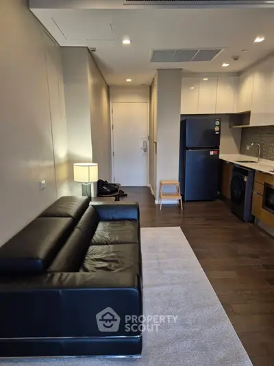 Modern apartment interior with sleek black sofa, compact kitchen, and stylish lighting.