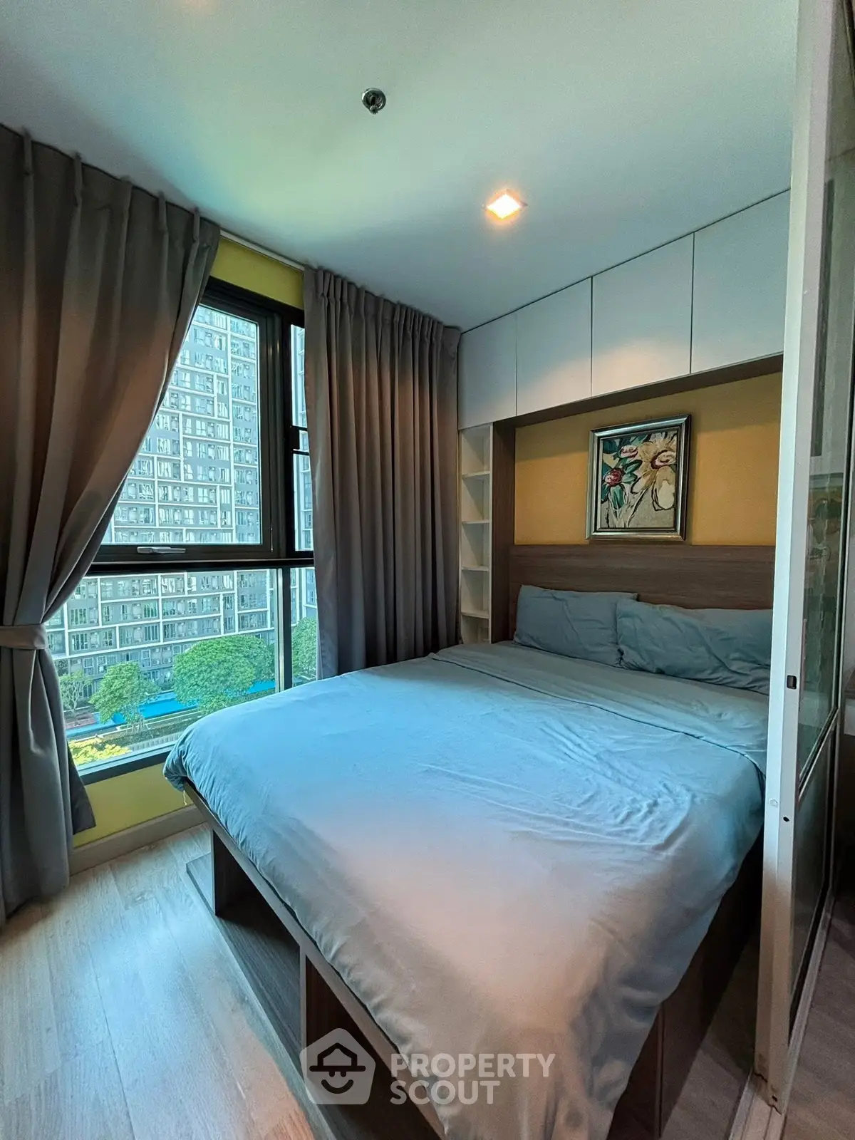 Cozy bedroom with large window offering stunning city view, modern decor, and ample natural light.
