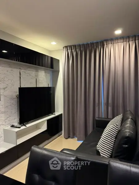 Modern living room with sleek black furniture and large TV, perfect for relaxation.