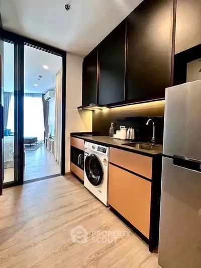 Modern kitchen with sleek cabinets, washing machine, and open layout leading to living area.
