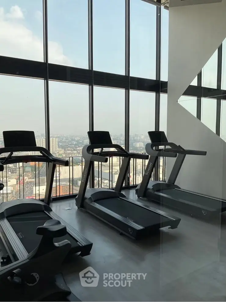 Modern gym with treadmills and panoramic city view in high-rise building.