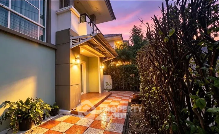 Charming exterior view of a modern home with a beautifully lit entrance and lush garden at sunset.