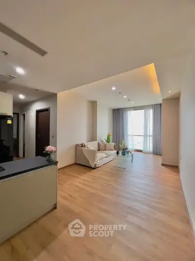Spacious modern living room with wooden flooring and large window view.