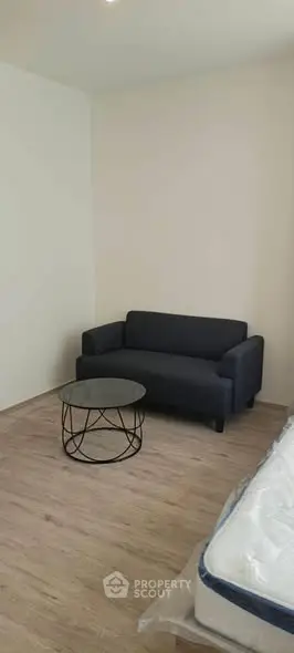 Cozy minimalist living room with modern black sofa and round glass coffee table on wooden floor.