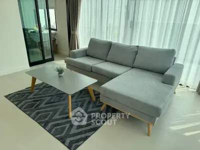 Modern living room with stylish gray sofa and geometric rug, flooded with natural light.