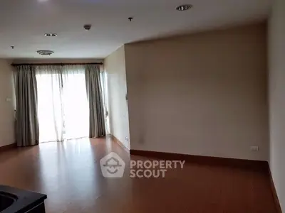 Spacious empty living room with wooden flooring and large window for natural light.