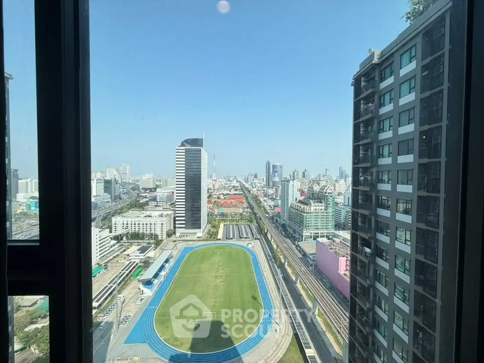 Stunning cityscape view from high-rise building window overlooking urban skyline and sports field.