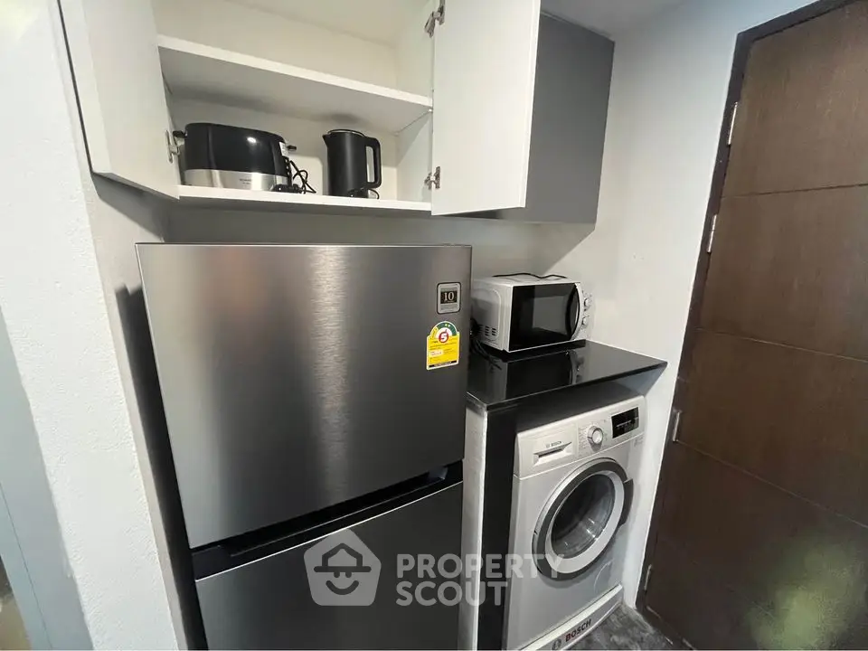 Modern kitchen with stainless steel fridge, washing machine, and microwave in compact layout.