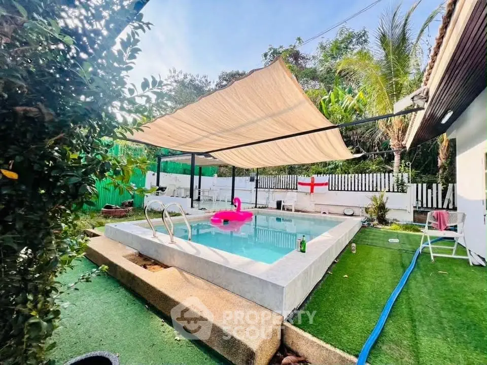 Charming backyard pool with sunshade and lush greenery, perfect for relaxation and entertainment.