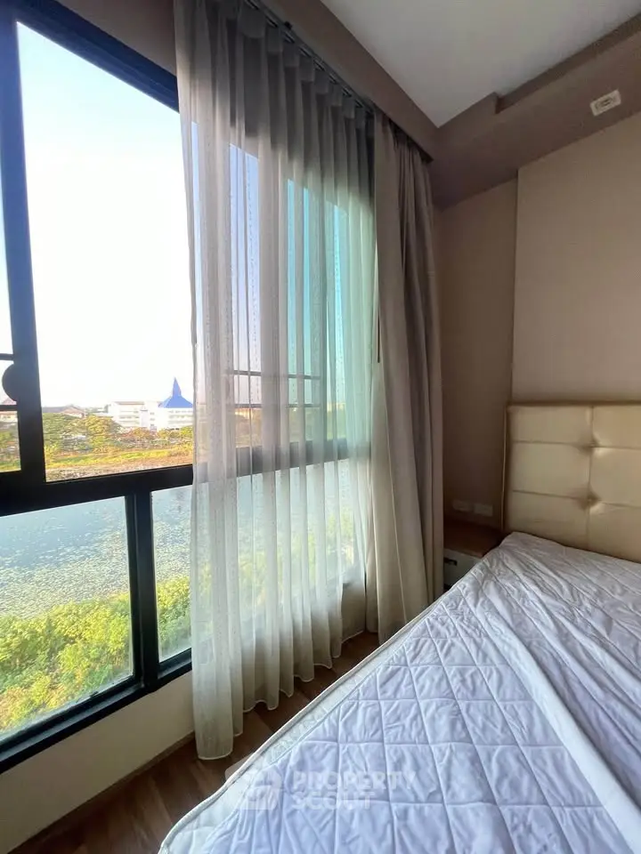 Bright bedroom with large window and scenic view, featuring elegant curtains and modern decor.