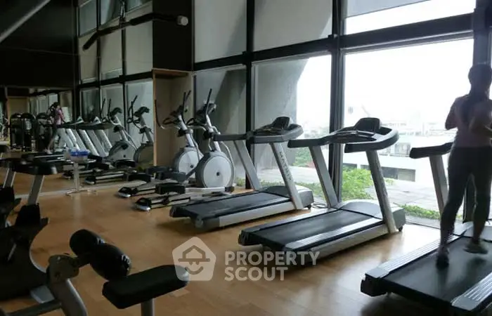 Spacious gym with modern equipment and large windows offering natural light.