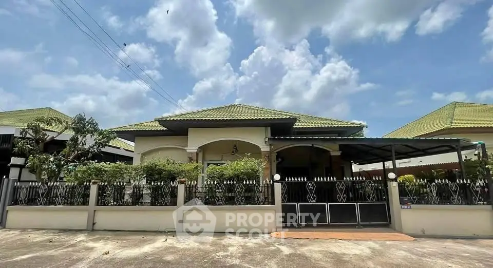 Charming single-story home with green roof and gated entrance under a bright blue sky.