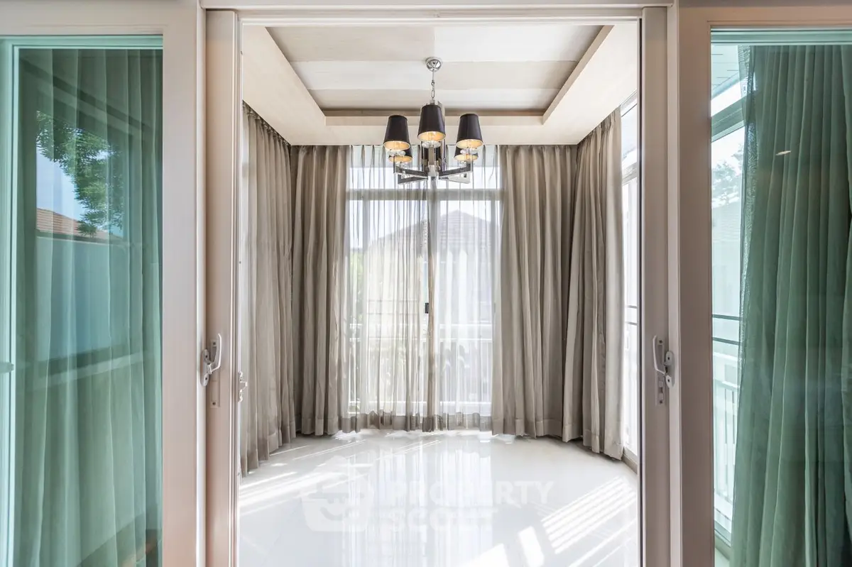 Sunlit spacious room with gleaming floor tiles, elegant chandelier, and floor-to-ceiling drapes opening to a serene balcony view.