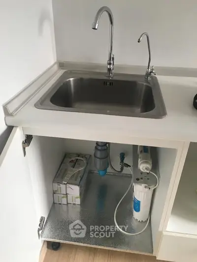 Modern kitchen sink with under-sink water filtration system in a sleek white cabinet.