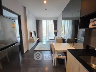 Modern living room with open kitchen and city view, featuring sleek furniture and large windows.