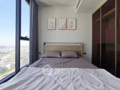 Modern bedroom with large window and city view, featuring stylish decor and cozy bedding.