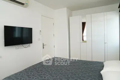 Modern bedroom with sleek white wardrobe and wall-mounted TV in a stylish apartment.