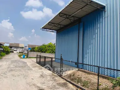 Industrial warehouse exterior with blue metal siding and fenced perimeter in a suburban area.