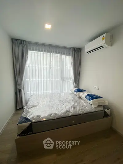 Modern bedroom with large window and air conditioning unit, featuring a new mattress and elegant curtains.