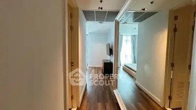 Spacious hallway leading to a modern bedroom with wooden flooring and large mirror.