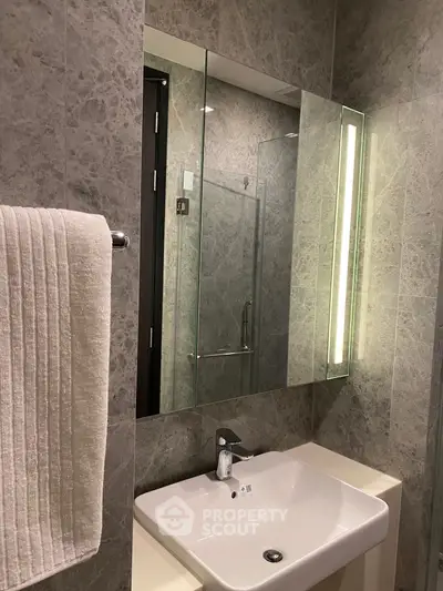Modern bathroom with sleek sink and illuminated mirror in elegant gray marble design.