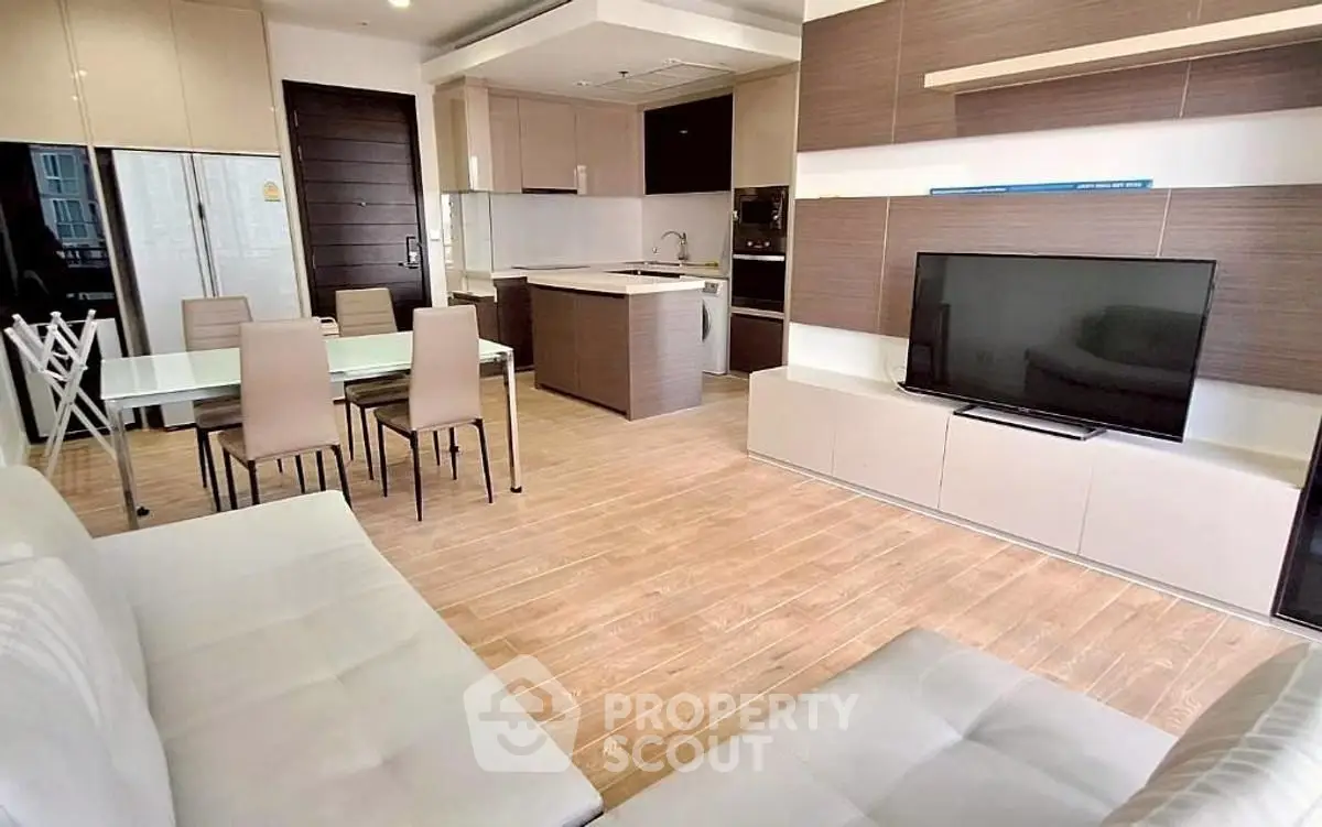 Modern open-layout living room with sleek kitchen and dining area, featuring contemporary furniture and wooden flooring.