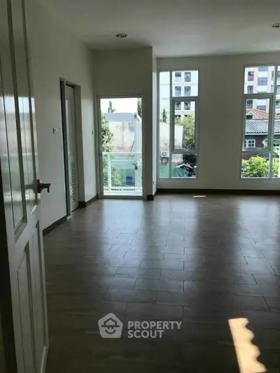 Spacious empty room with large windows and wooden flooring, offering abundant natural light.