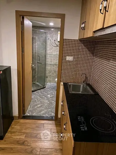 Compact kitchen with modern appliances and adjacent bathroom in cozy apartment.