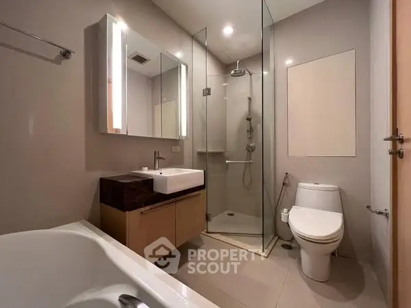 Modern bathroom with glass shower, bathtub, and sleek fixtures.
