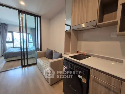 Modern apartment interior with compact kitchen and cozy living area, featuring a sliding glass door to the bedroom.