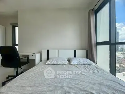Modern bedroom with large windows offering city views and a cozy workspace.