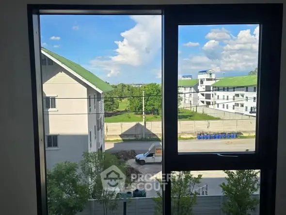 Scenic view from a window overlooking residential buildings and lush greenery.
