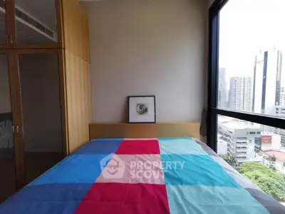 Modern bedroom with colorful bedding and city view from large window.