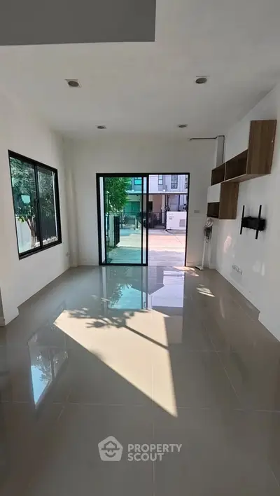 Spacious modern living room with large windows and sliding glass doors leading to a patio, featuring sleek tile flooring.