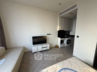 Modern studio apartment with sleek kitchen and cozy living area, featuring a washing machine and minimalist decor.